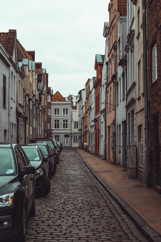 cars parked on side of the road in between buildings during daytime in Lübeck Germany