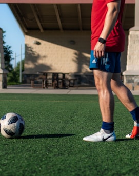 man in red shirt and blue shorts playing soccer during daytime