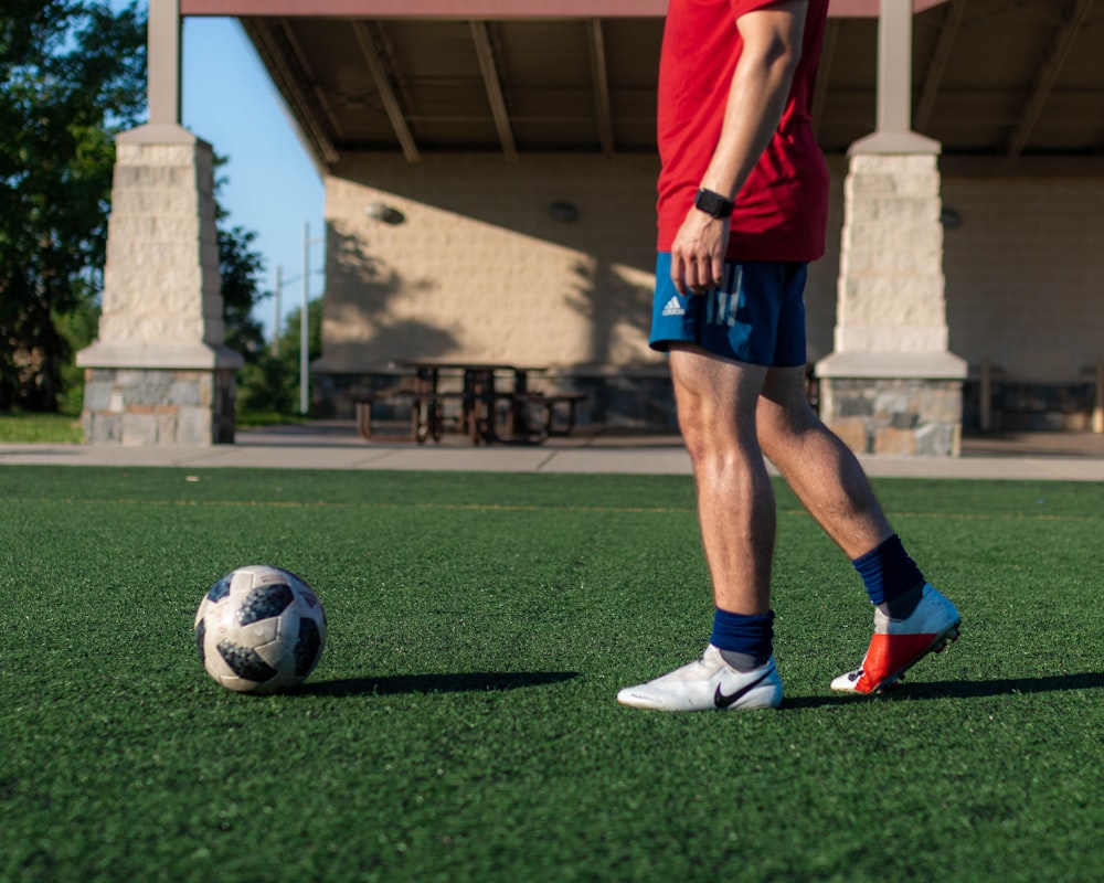 man in red shirt and blue shorts playing soccer during daytime