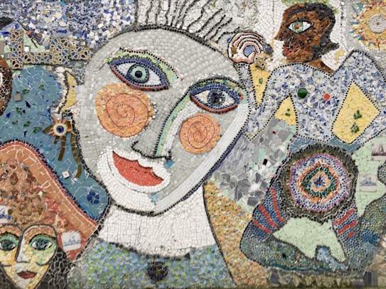 A vibrant mosaic artwork featuring abstract human figures with exaggerated facial features, including large spiral eyes and colorful, textured patterns. The piece combines various small tiles in blues, whites, oranges, and greens to create a dynamic and whimsical aesthetic.