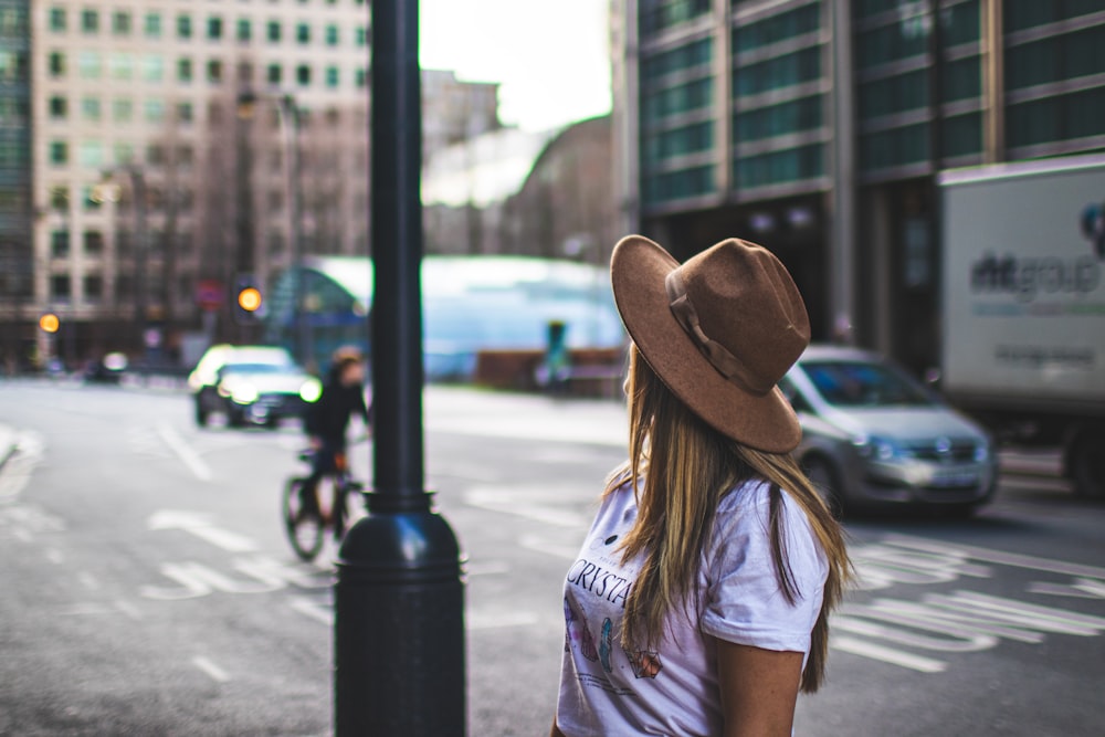 woman in blue t-shirt wearing brown fedora hat standing near road during daytime