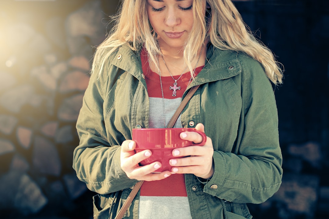 woman in green zip up jacket holding red ceramic mug