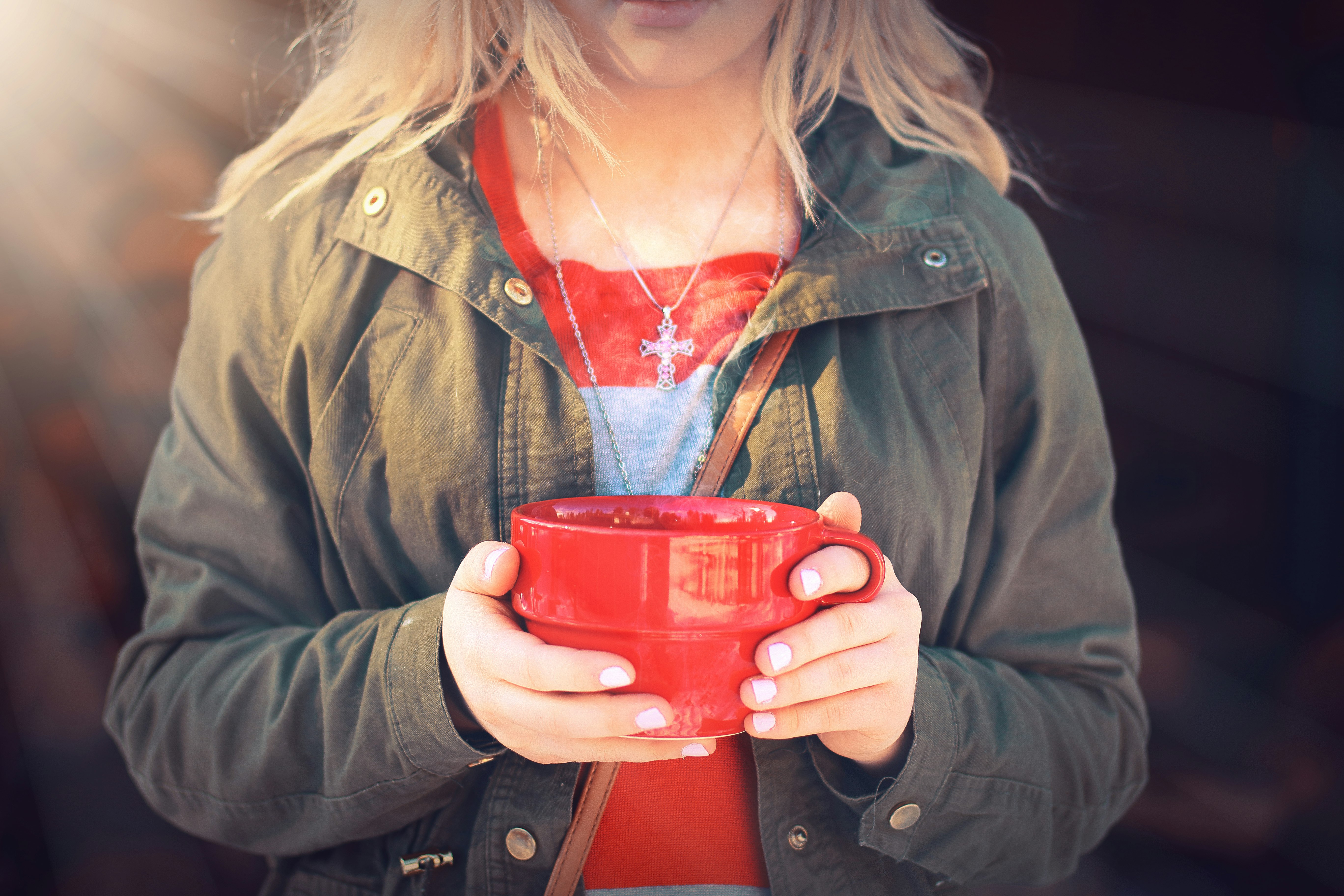 woman in green jacket holding red ceramic mug