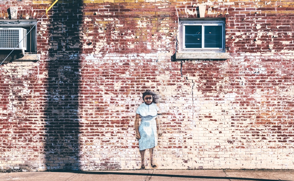girl in white dress standing beside brown brick wall during daytime