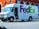 A FedEx Ground delivery truck is parked on a street next to a red brick building. The truck is white with the FedEx logo prominently displayed in purple and green on the side. A driver is seated inside, visible through the open door.