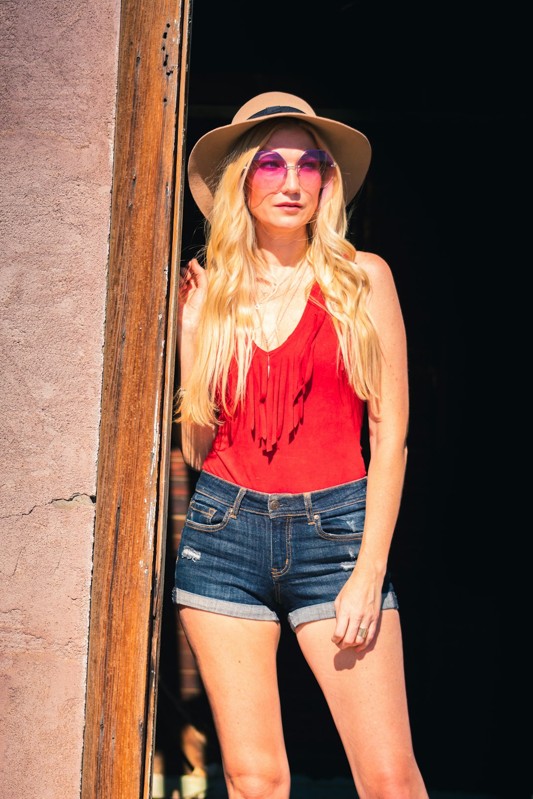 woman in orange tank top and blue denim shorts wearing brown cowboy hat