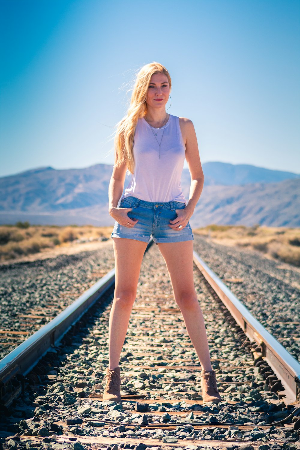 donna in pantaloncini di jeans blu in piedi sulla rotaia del treno durante il giorno