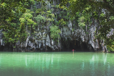 person in red shirt standing on rock in the middle of lake during daytime