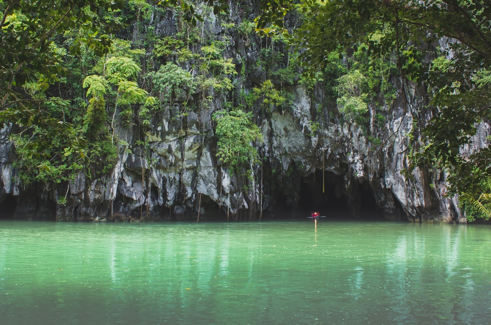 person in red shirt standing on rock in the middle of lake during daytime