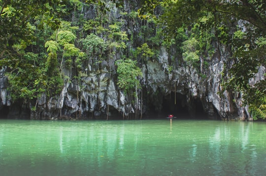 person in red shirt standing on rock in the middle of lake during daytime in Puerto Princesa Subterranean River National Park Philippines