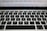 A close-up view of a laptop keyboard featuring a QWERTY layout with black keys and white lettering. Above the keyboard, there is a blurred view of the laptop screen displaying text.