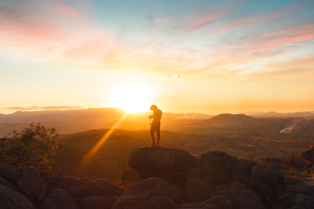 Silueta del hombre de pie sobre la roca durante la puesta del sol