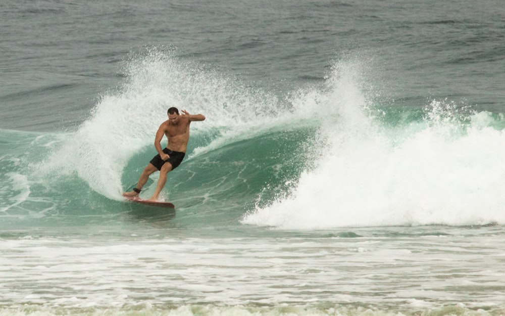 Mann in schwarzen Shorts beim Surfen auf Meereswellen tagsüber