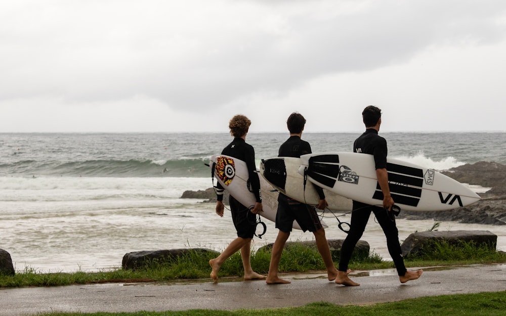 2 men carrying white surfboard walking on beach during daytime