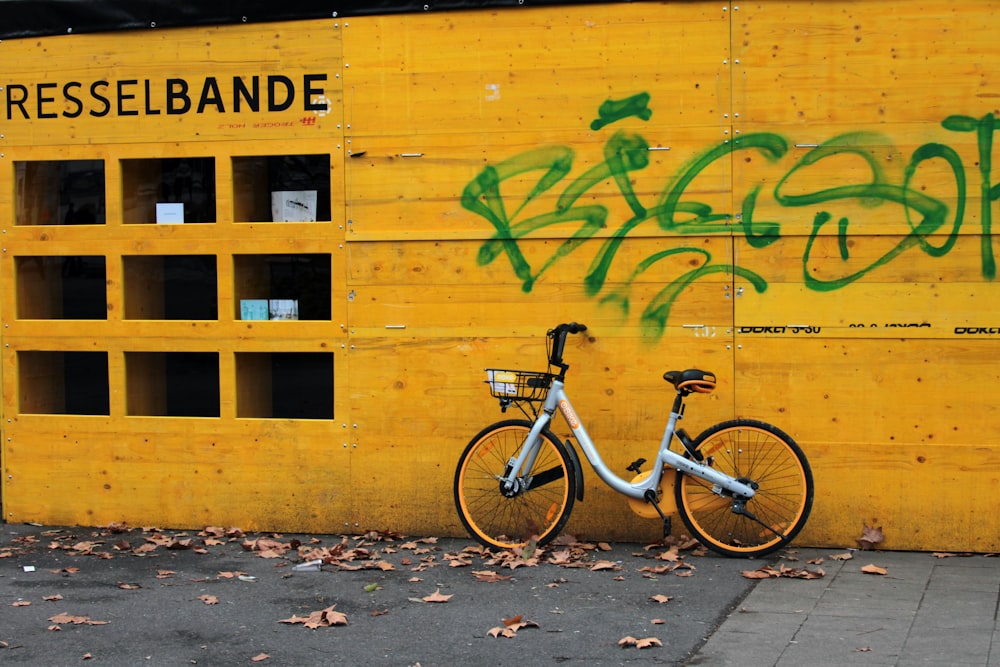 white and black commuter bike parked beside yellow wall