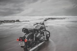 Motorbike parked on a coastal road in Europe with waves crashing nearby under a cloudy sky.
