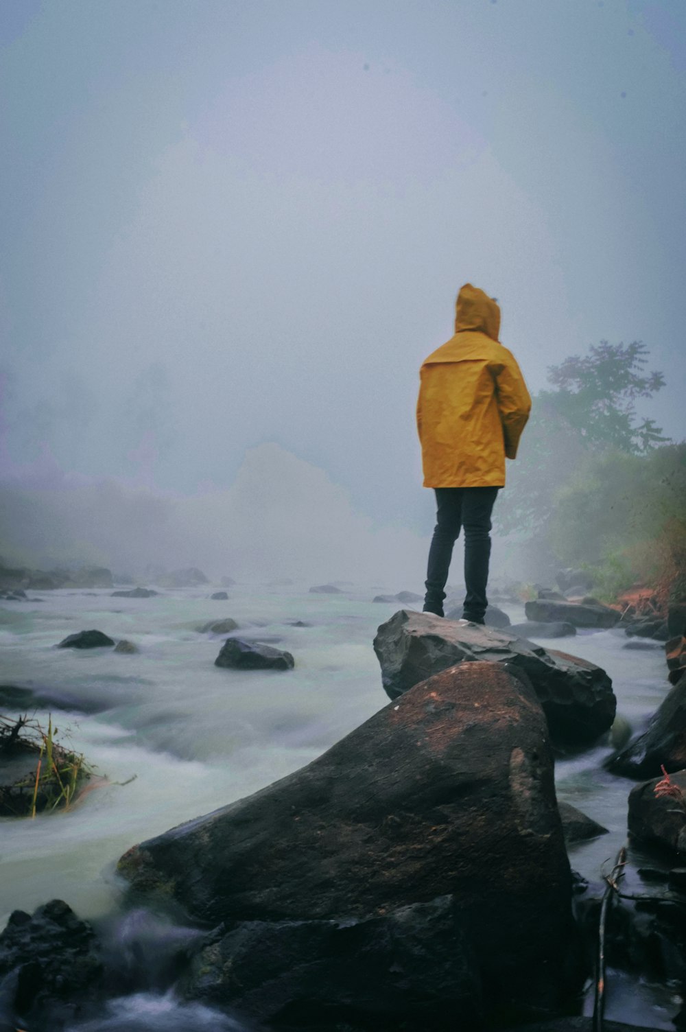 person in brown coat standing on rock near body of water