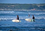2 women in black wet suit riding white surfboard on sea during daytime