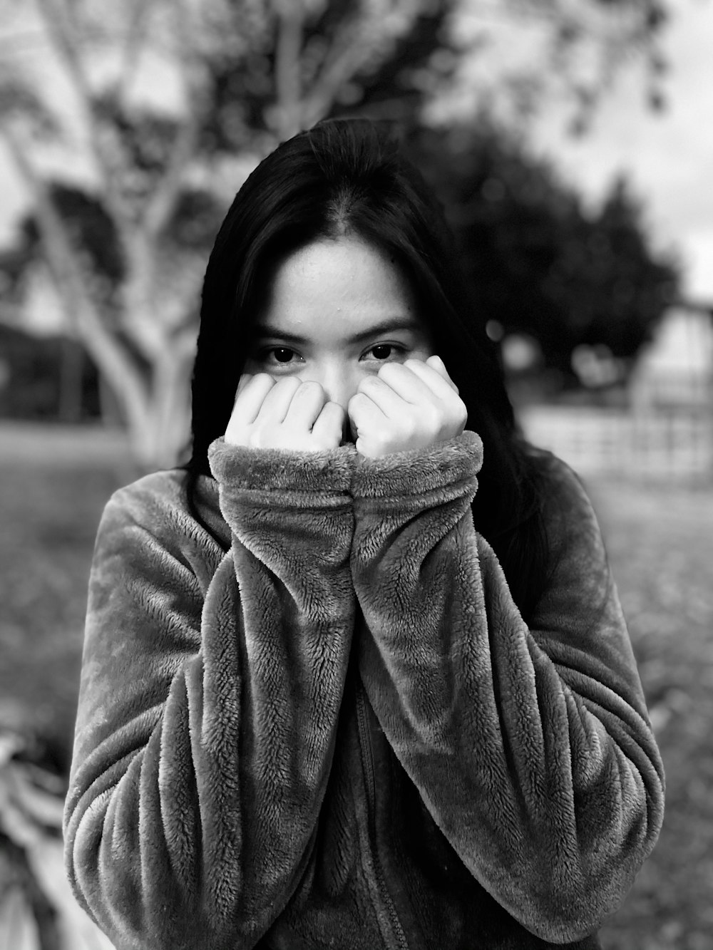 grayscale photo of woman in sweater covering her face with her hand
