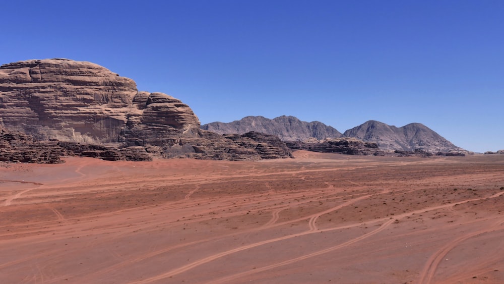 brown sand field near brown rocky mountain under blue sky during daytime