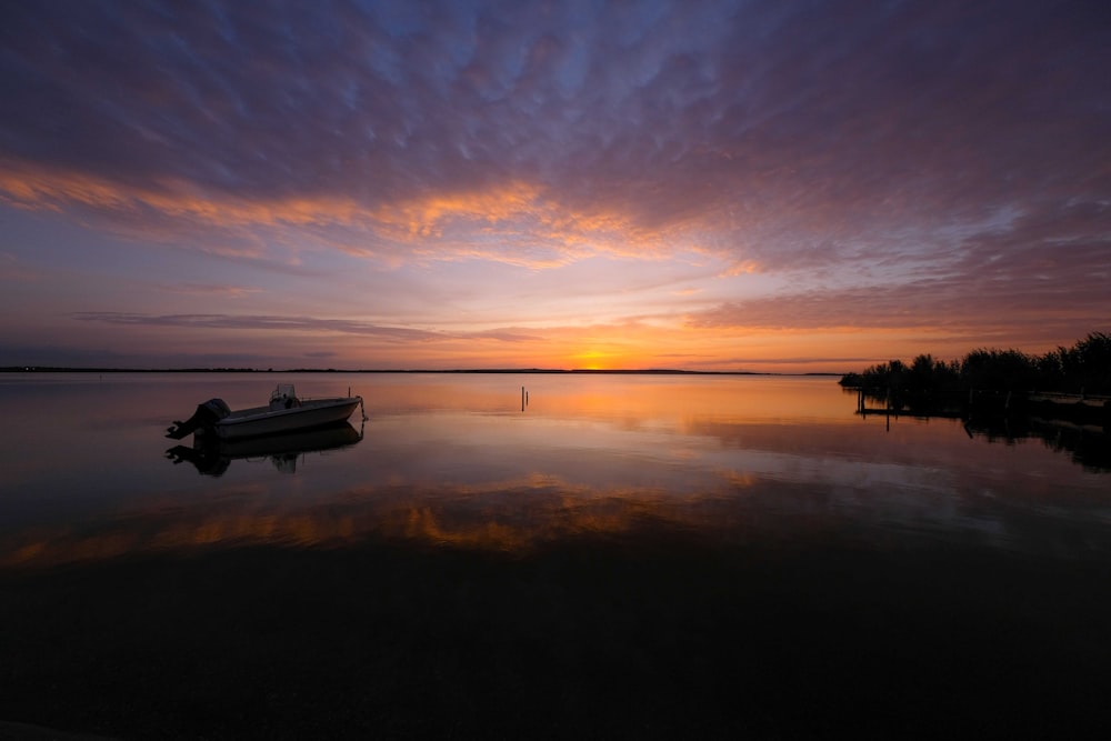 silhouette of boat on calm water during sunset