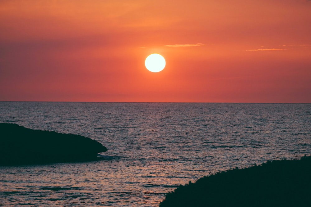 silhouette of rock formation on sea during sunset