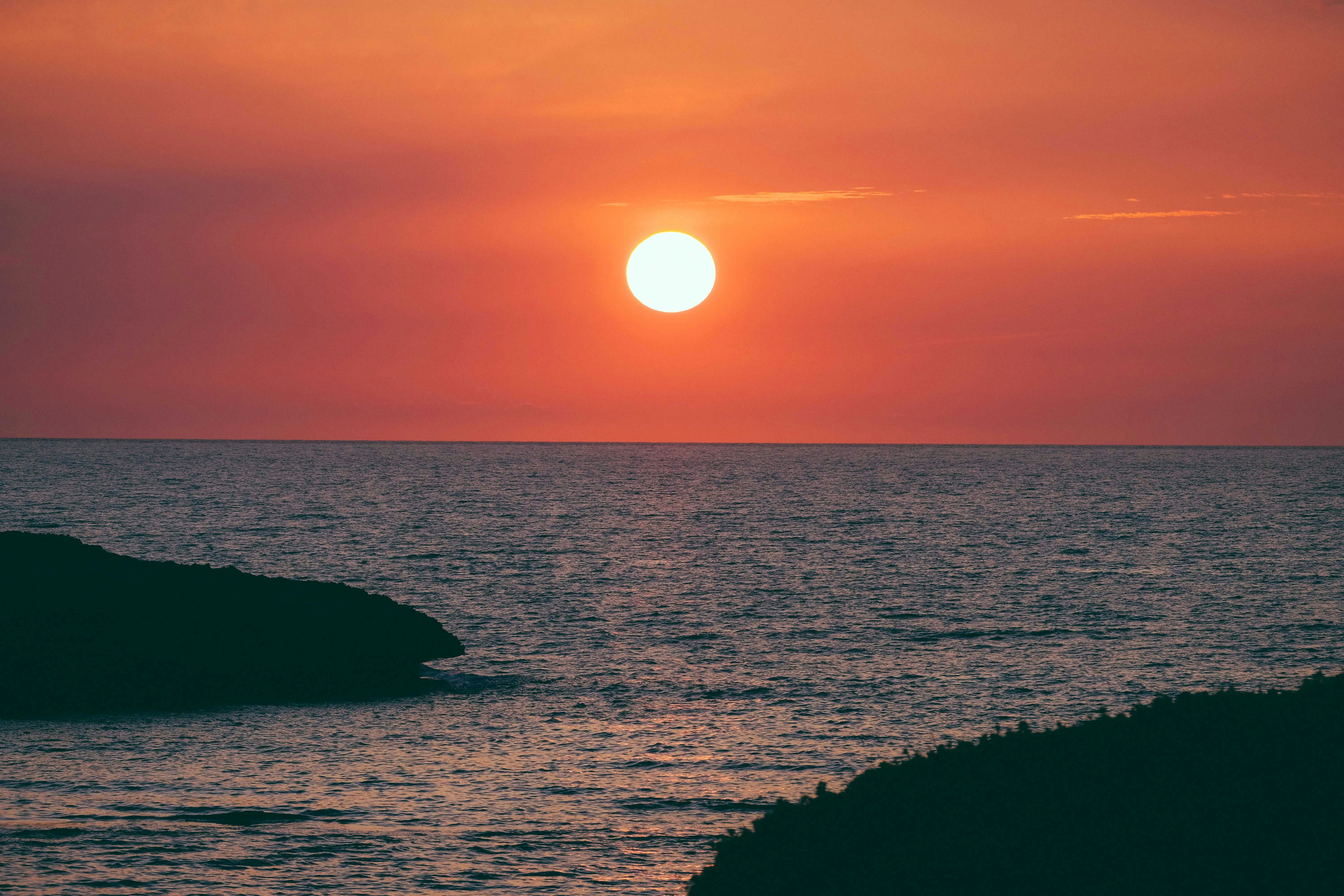 silhouette of rock formation on sea during sunset