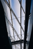 A modern architectural structure with a glass ceiling and metal frames. The ceiling allows natural light to filter through, creating a bright and airy atmosphere. The geometric lines of the framework add an industrial and contemporary aesthetic.