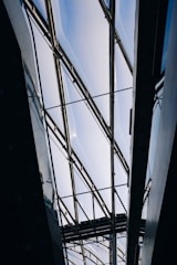 A modern architectural structure with a glass ceiling and metal frames. The ceiling allows natural light to filter through, creating a bright and airy atmosphere. The geometric lines of the framework add an industrial and contemporary aesthetic.