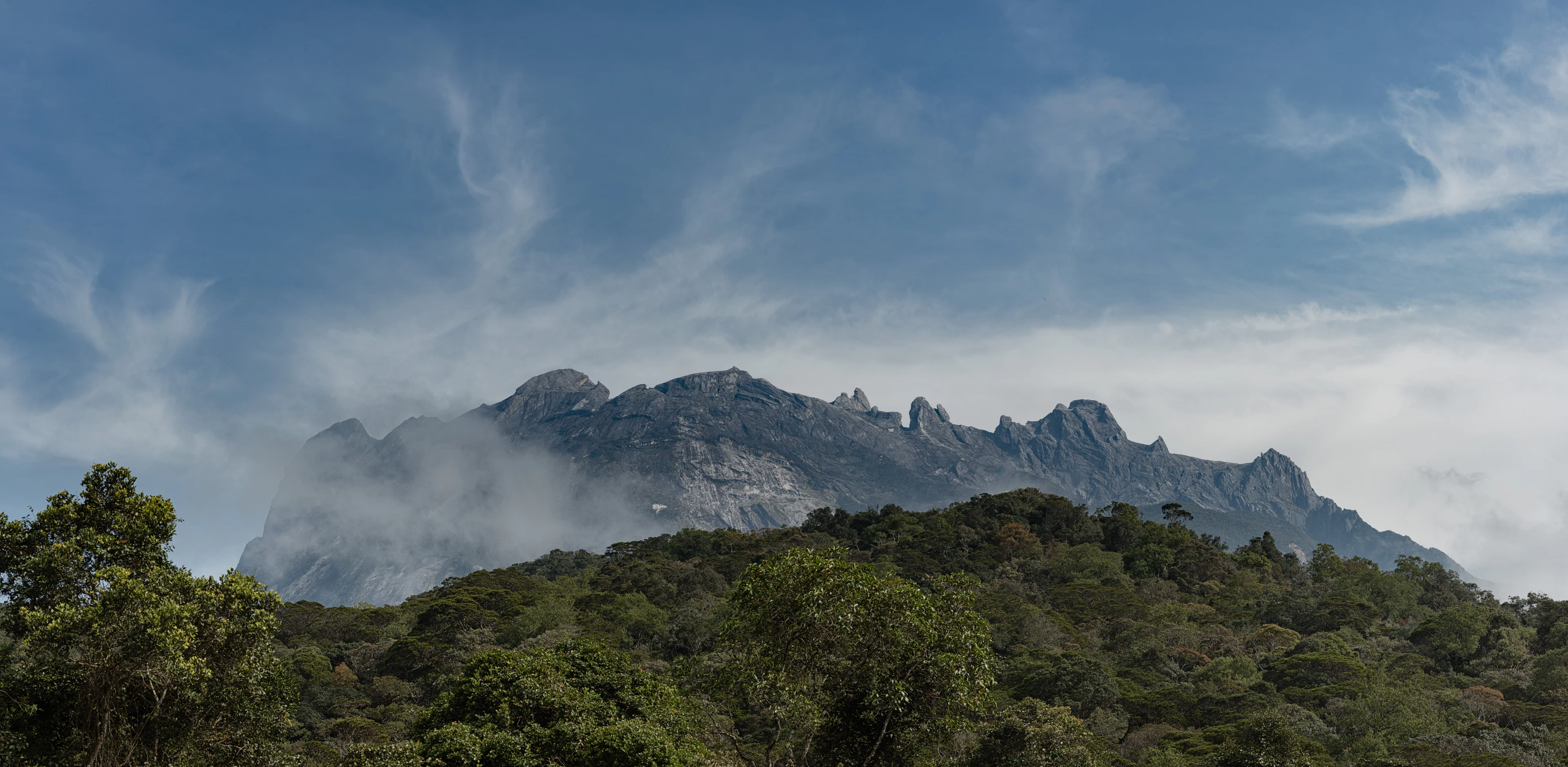 The granite ridges of Mount Kinabalu above forested hills and cloud, Sabah