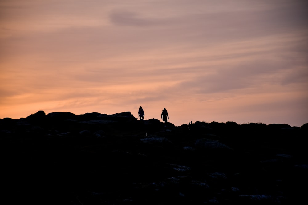 silhouette of people on rocky mountain during sunset