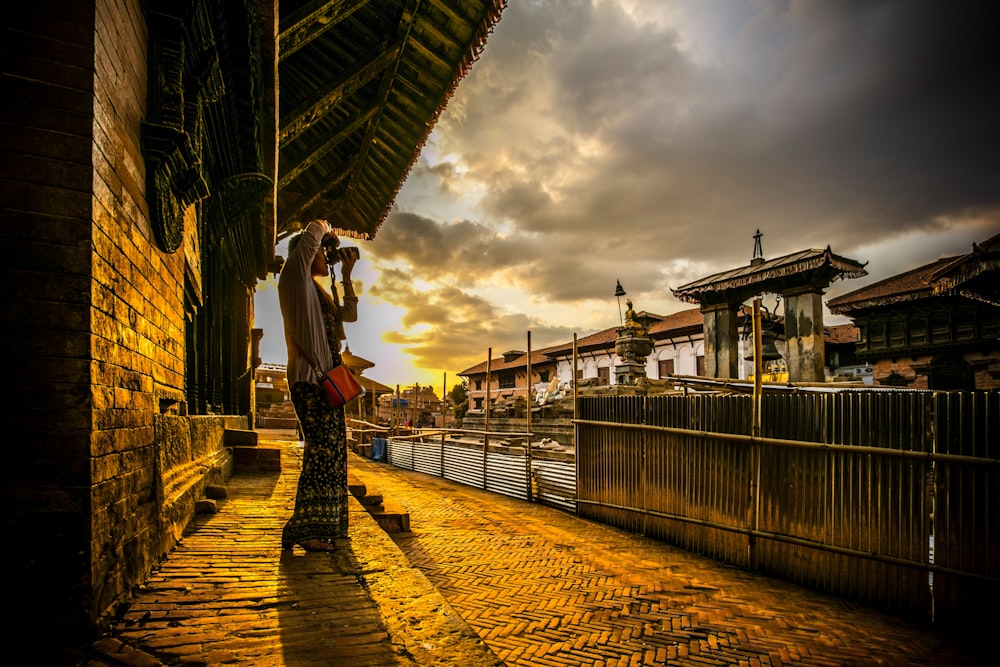 woman in white long sleeve shirt and black skirt standing on brown wooden dock during sunset