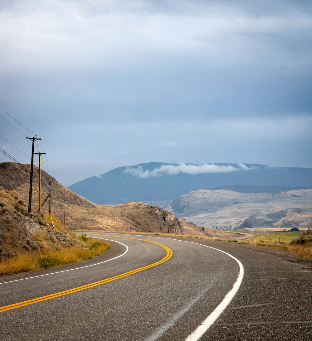 gray concrete road near brown mountain under blue sky during daytime