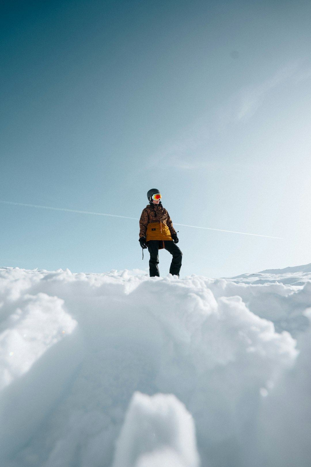 person in brown jacket and black pants walking on snow covered ground under blue sky during