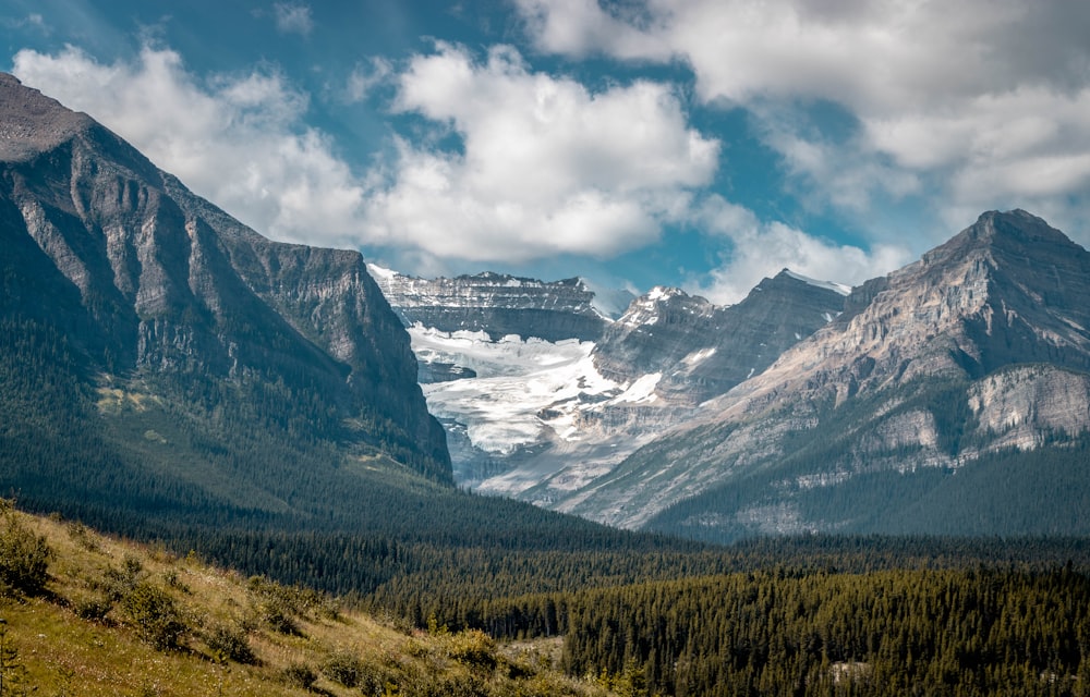 green trees near snow covered mountain under white clouds and blue sky during daytime