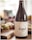 A bottle of wine labeled 'Estel Mallorca 2015' is placed prominently in the foreground. The label features a constellation motif with black dots and lines on a white background. Behind the bottle, there is a blurred, inviting spread of snacks or appetizers, set on a wooden board and partially visible, suggesting a casual dining or gathering atmosphere.