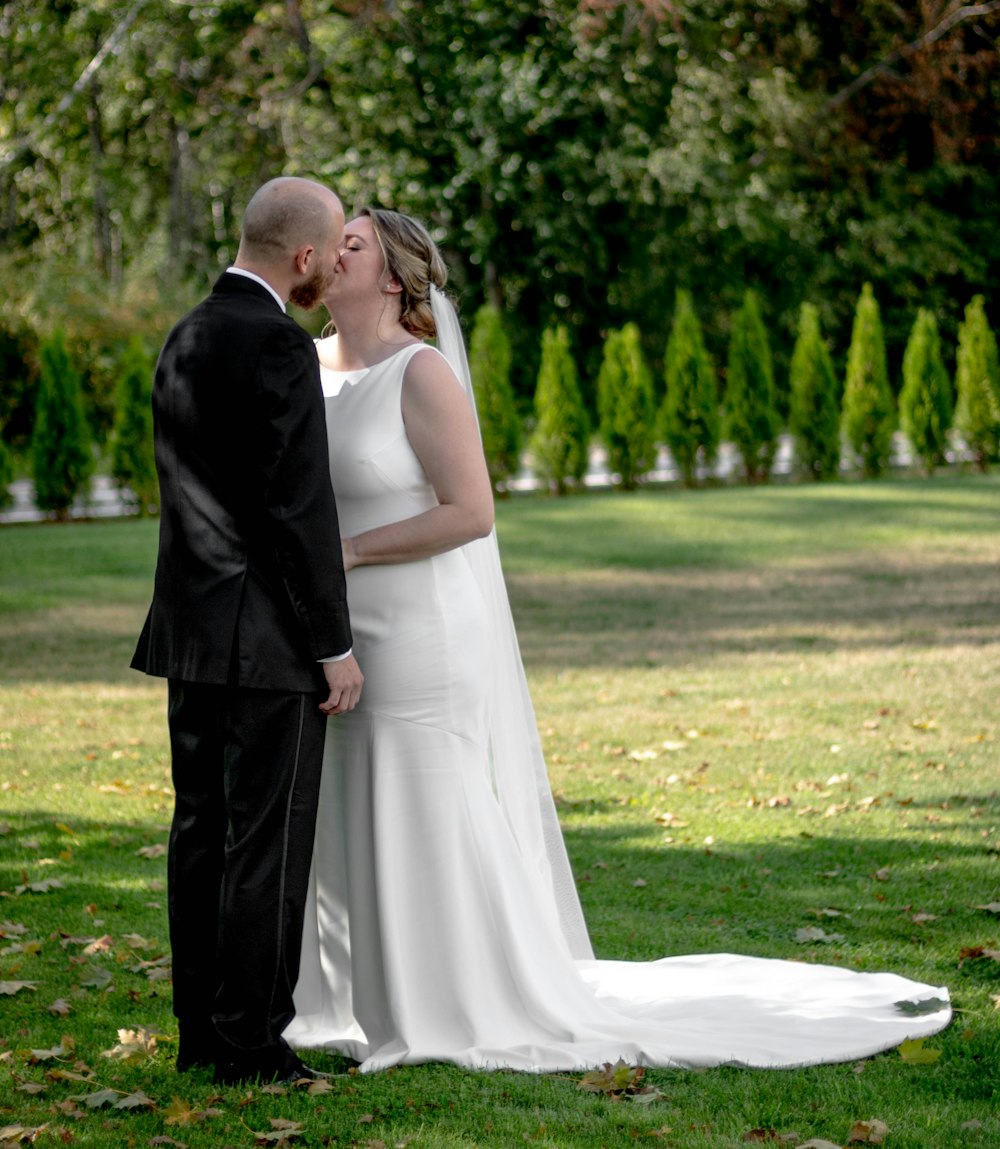 man in black suit and woman in white wedding dress walking on green grass field during