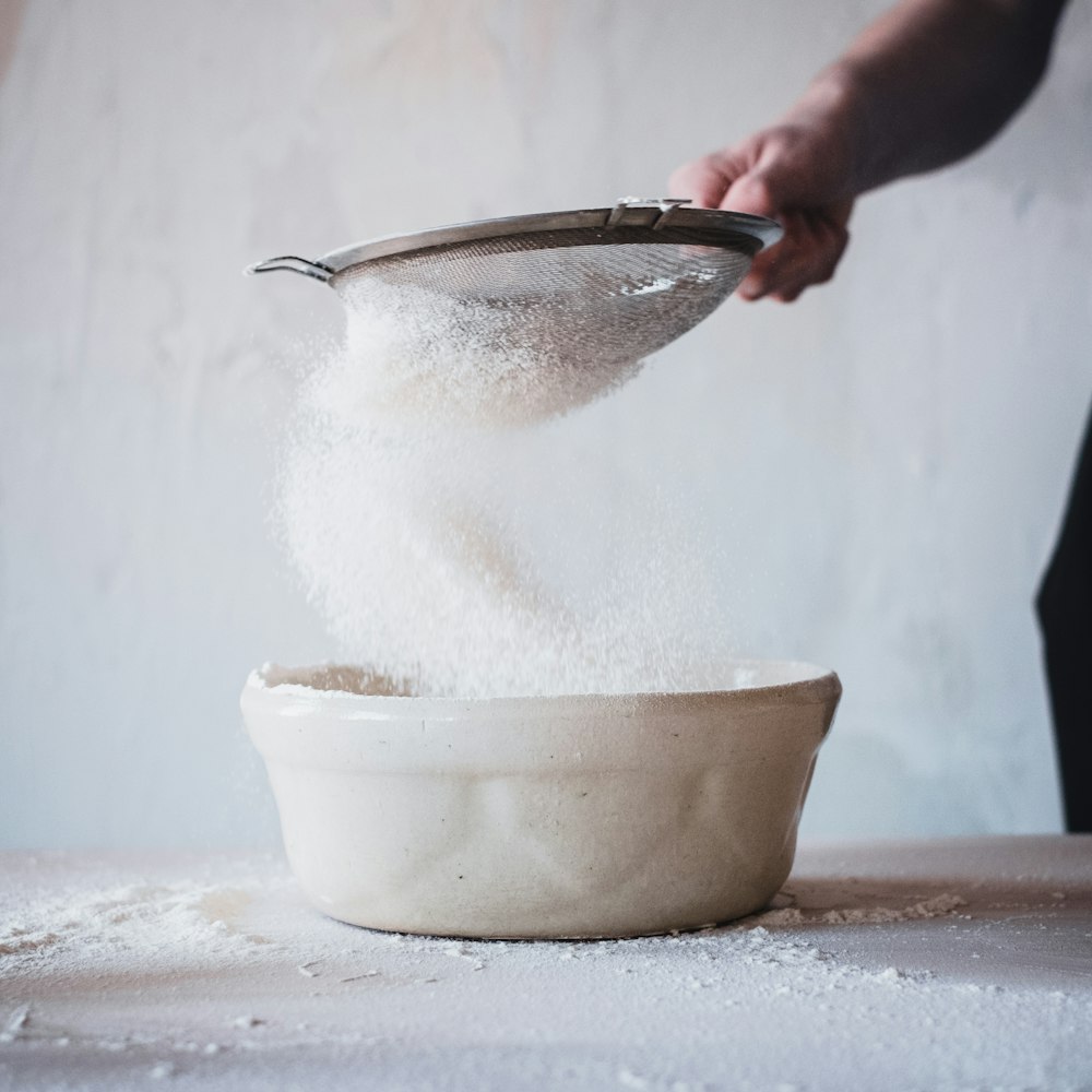 person pouring water on white ceramic bowl