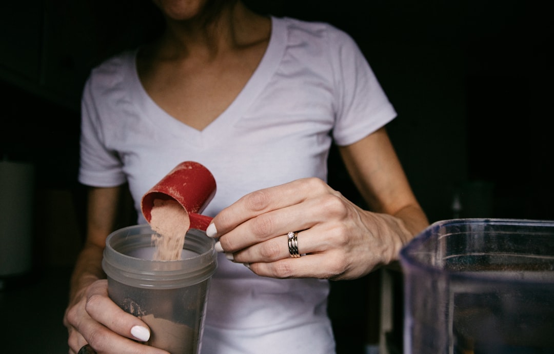 woman in white v neck shirt holding red heart shaped lollipop, Morning Routine: Hands adding protein shake powder to a c