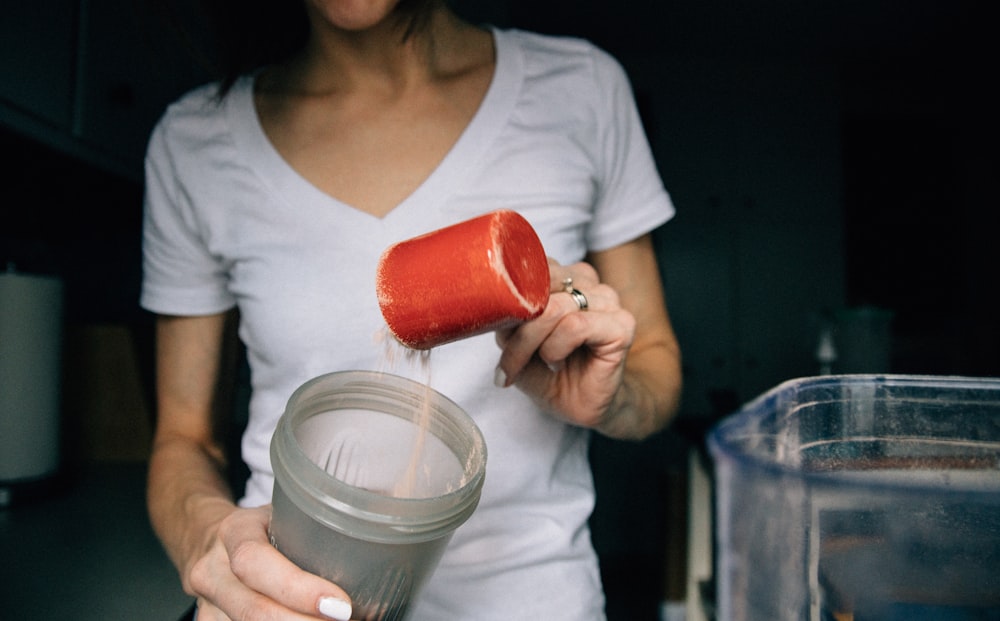 Mujer con camiseta blanca de cuello redondo sosteniendo un vaso de plástico rojo