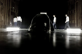 A dimly lit rehearsal room with actors mid-performance, shadows casting dramatic shapes on the walls.