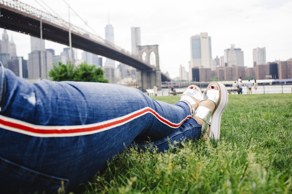 person in blue denim jeans and white sneakers sitting on green grass during daytime