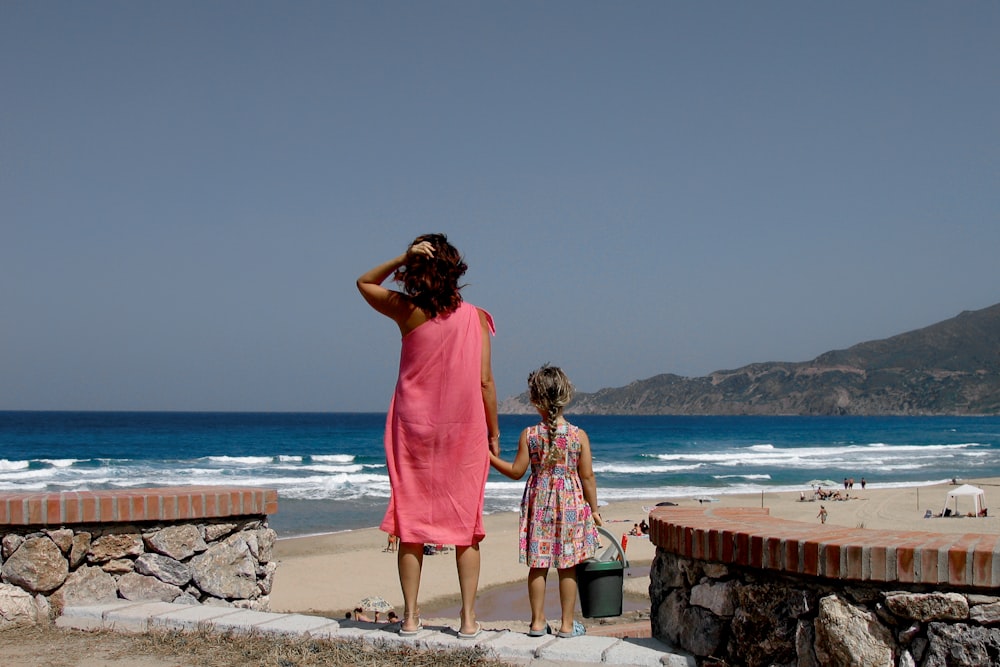 昼間、水辺の茶色のコンクリートレンガの上に立つ2人の女性