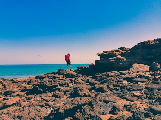 man in red shirt standing on rock formation near sea during daytime in Hormuz Island Iran