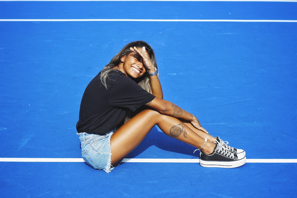 woman in black shirt and blue denim shorts sitting on blue floor