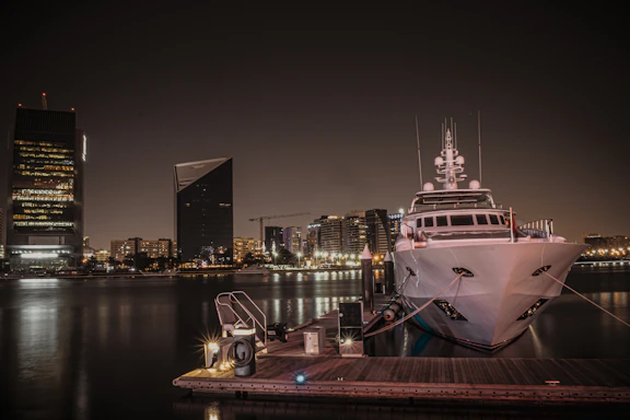 A sleek luxury yacht anchored at Dubai Marina during golden hour with city skyline in the background.