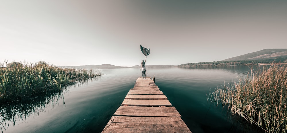 person in black shirt and blue denim jeans standing on brown wooden dock during daytime