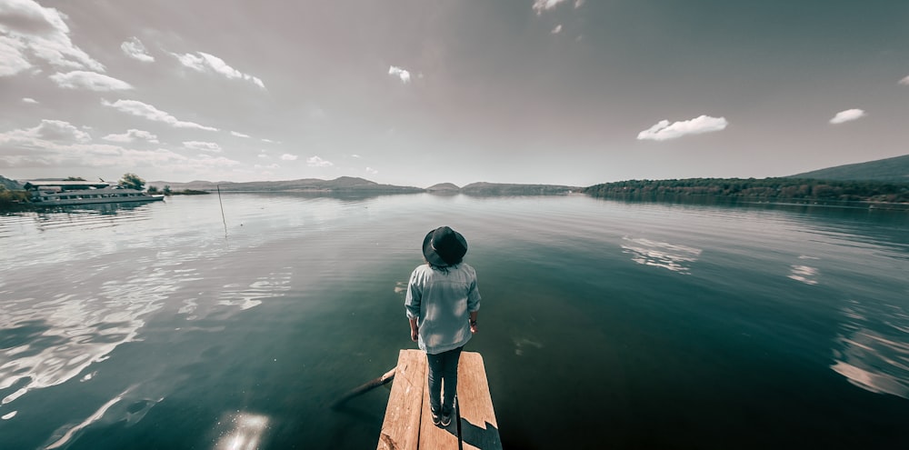 person in gray hoodie sitting on brown wooden dock during daytime