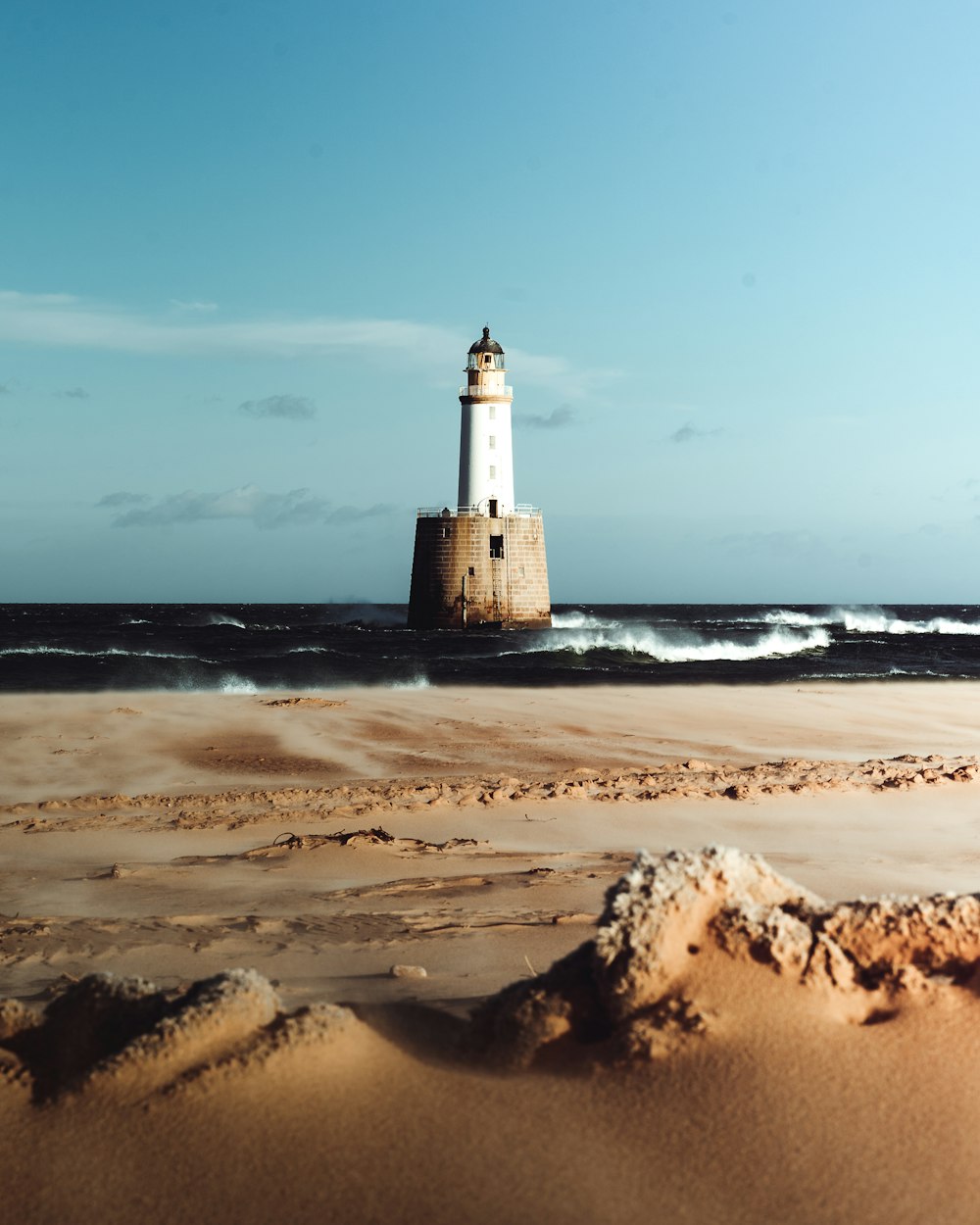 white and black lighthouse on brown sand near body of water during daytime
