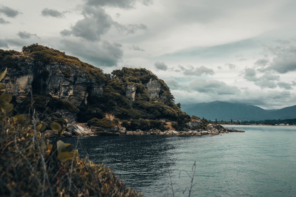 body of water near mountain under cloudy sky during daytime